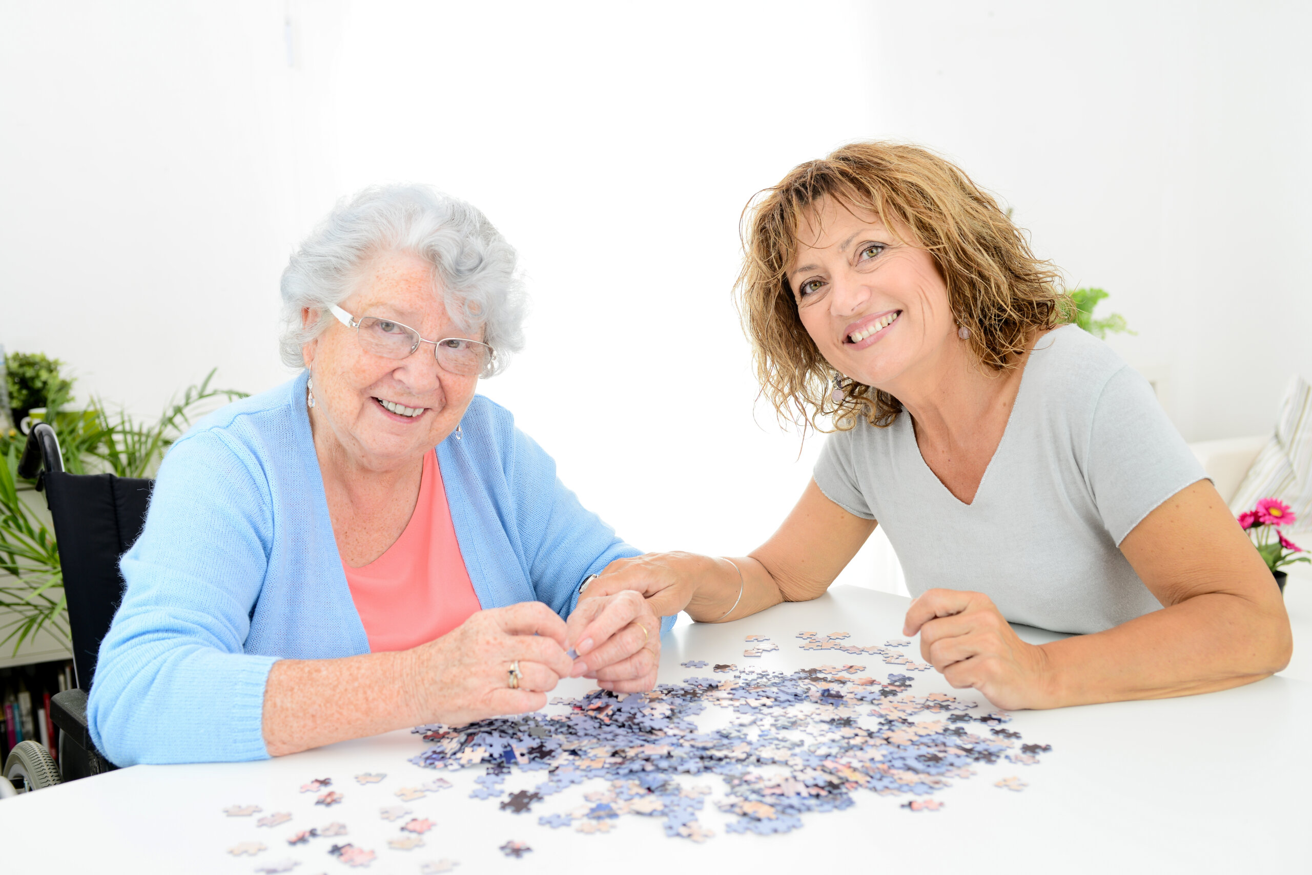 cheerful mature woman doing a puzzle and spending time with elderly senior woman at home